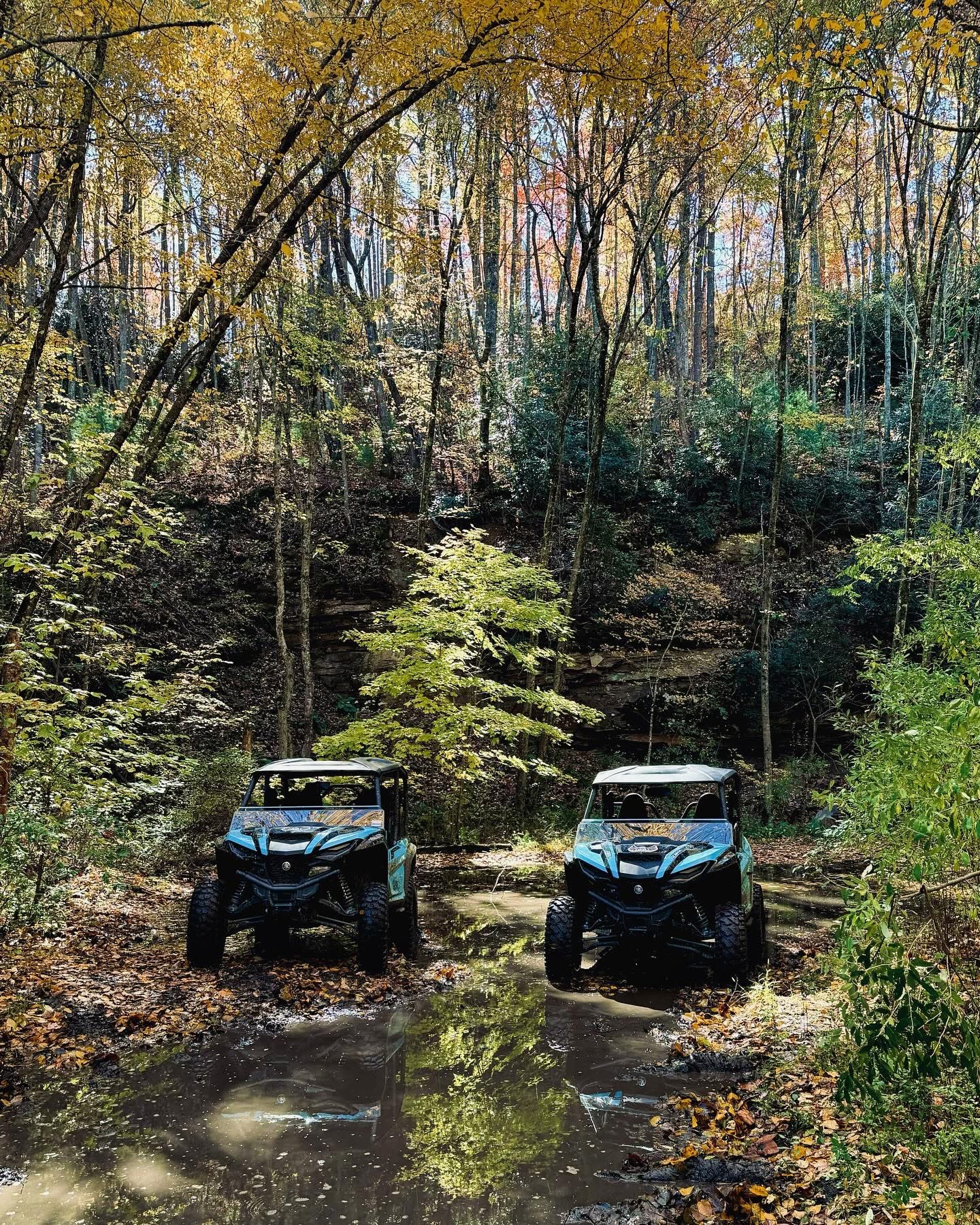 Two side-by-sides parked in a shallow creek surrounded by fall foliage